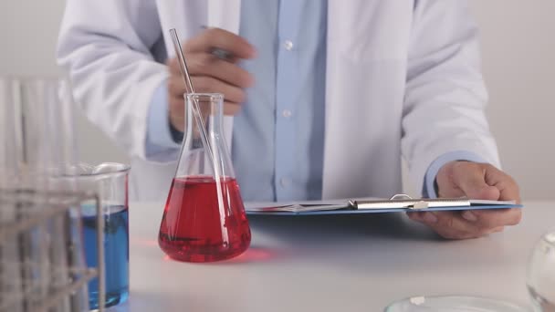 穿着实验室外套的年轻科学家撰写实验结果和搅拌红色溶液 科沃那病或科沃德病实验室工作的科学家 — 图库视频影像