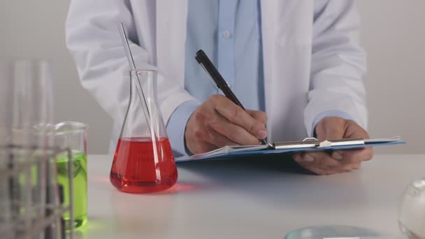 Homem Jovem Cientista Revestimento Laboratório Escrevendo Resultados Experimentais Verifique Solução — Vídeo de Stock