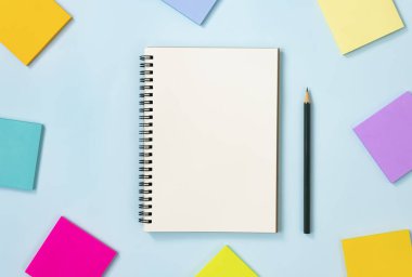 Spiral Notebook ya da Spring Notebook in Unline Type and Multi Color Sticky Note and kalem on Blue Pastel Minimalist Arkaplan. Orta Çerçevede Spiral Not Defteri Model