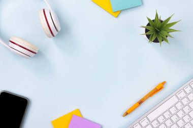 Modern Temiz Yaratıcı Ofis Masası veya Masası Üst Görünüm veya Düz Yatay ve Kırtasiye Klavye, Kulaklık, Kalem, Yapışkan Not, Ofis Bitkileri, Cep Telefonu. Minimalist Özgeçmiş ve Ofis Malzemeleri