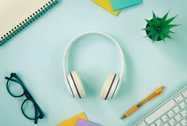 Headphone at Center and Office Supplies as Keyboard,Pen,Sticky Note,Office Plants,Glasses,Spiral Notebook on Modern Clean Creative Office Desk or Table on Top View or Flat Lay in Vintage Tone