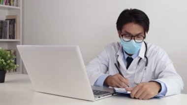 Laboratuvar önlüklü ya da steteskoplu genç Asyalı doktor gözlük takıyor ve maske takıyor Hasta Muayenesi Raporu Ofiste
