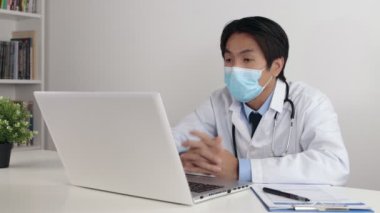 Laboratuvar önlüklü genç Asyalı doktor ya da steteskop takan cüppeli maskeli hasta Video Sohbet ya da Ofiste Görüntü Çağrısı