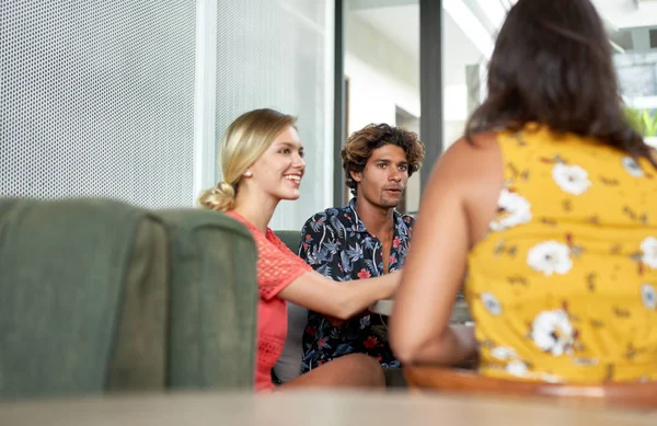 Disparo cándido de tres amigos multiétnicos sentados juntos a la mesa en un luminoso café de moda que sirve café de comercio justo con ropa de moda — Foto de Stock