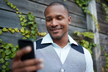 Yakışıklı siyah adam dışarı asılı, ahşap bir çit yanında dışında onun hareket eden smartphone ile mesaj