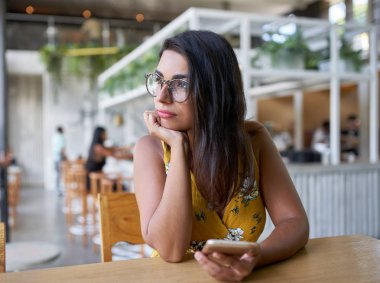 Güzel İspanyol milenyal kadın Candid yaşam portre bitkiler ile modern trendy ve parlak kahve mağazasında cep telefonu tutan pencere bakıyor