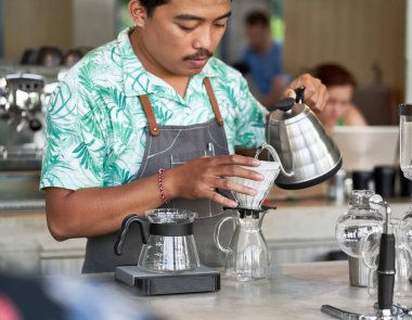 Gülümseyen etnik Endonezya barista ve küçük iş sahibi parlak trendy kahve dükkanı önlük giyen organik Fuar-Ticaret kahve hazırlanıyor Candid yaşam çekimi