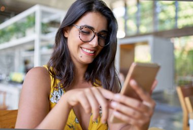 Bitkiler ile modern trendy ve parlak kafede cep telefonunda yazarak gülüyor İspanyol milenyal Blogger Candid yaşam tarzı portre