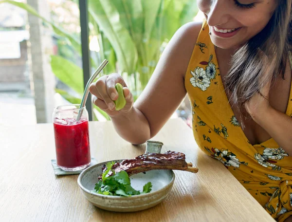 Closeup lifestyle portrait shot of a smiling ethnic woman eating healthy organic grass-fed beef ribs and herbs drinking juice — Stock Photo, Image