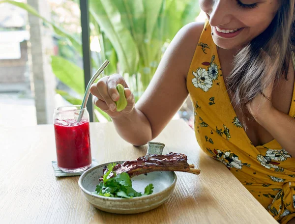 Nahaufnahme Portrait einer lächelnden ethnischen Frau, die gesunde, mit Gras gefütterte Rinderrippen und Kräuter isst und Saft trinkt — Stockfoto