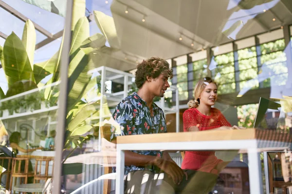 Lifestyle shot of two candid young diverse multi-ethnic millennials working and meeting together in a bright tropical restaurant office space