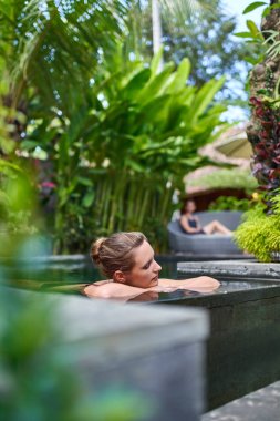 Bali tropikal tatil sırasında lüks otelin güneşli ve yemyeşil taş yüzme havuzunda açık havada rahatlatıcı Oldukça huzurlu bir kadın