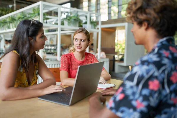 Aufrichtiges Lifestylebild einer multiethnischen Millennial-Kollegengruppe, die gemeinsam am Laptop an einem Tisch in einem hellen modernen Café diskutiert — Stockfoto