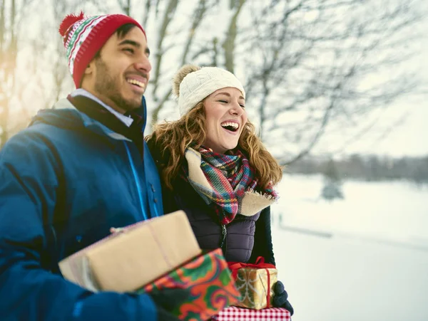 Smiling diverse couple holding Christmas presents while walking through a winter forest — Stock Photo, Image