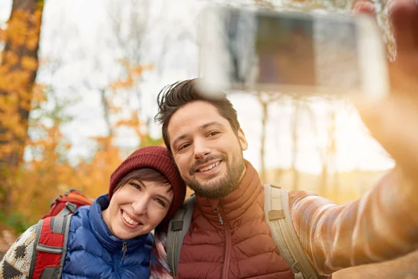 Couple of Canadian millennials taking selfies with a smartphone in a fall forrest — Stock Photo, Image