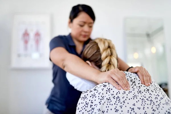 Chinesische Masseurin gibt einer attraktiven blonden Kundin an ihrem Arbeitsplatz in einem hellen Büro eine Nacken- und Rückendruckbehandlung — Stockfoto