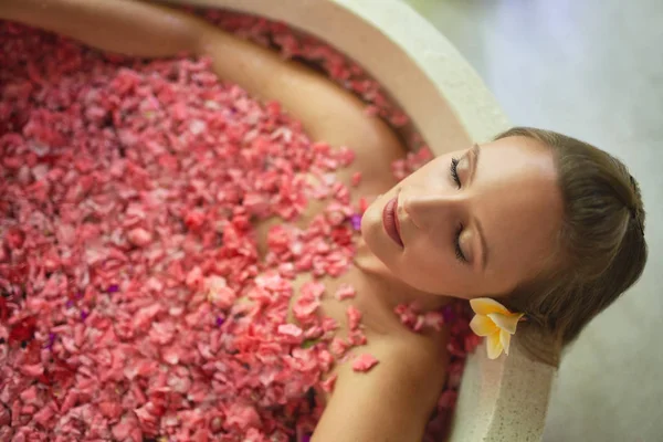 Overhead shot of natural millennial woman in luxurious spa bathtub filled with flower petals in tropical resort and wellness centre — Stock Photo, Image