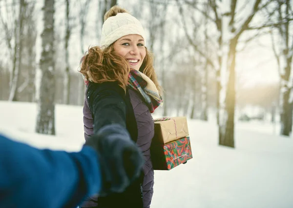 Фотография разношерстной пары, держащей рождественские подарки во время прогулки по зимнему лесу — стоковое фото