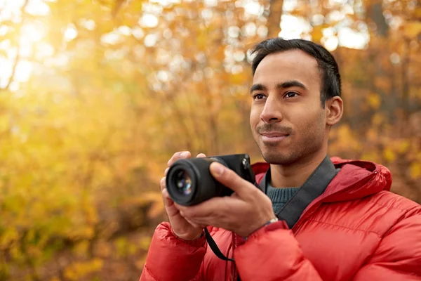 Atractivo hombre indio tomando fotos con una cámara sin espejo a través del bosque en el otoño en Canadá — Foto de Stock