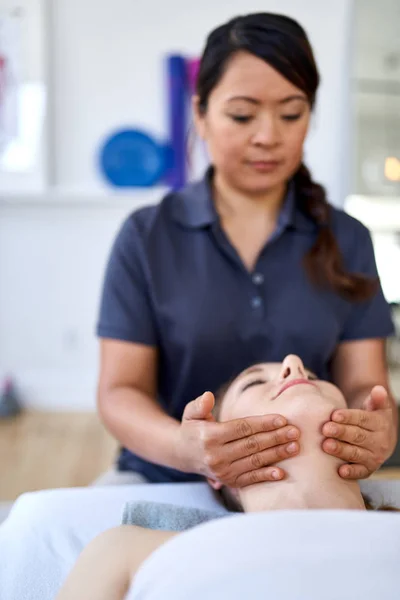 Chinese vrouw massage therapeut geven een behandeling aan een aantrekkelijke blonde cliënt op massagetafel in een lichte medische kantoor — Stockfoto