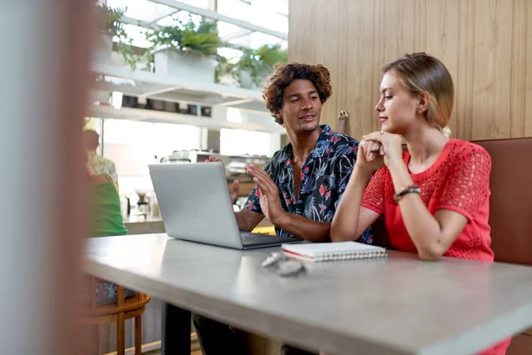 Candid lifestyle shot of attractive multi-ethnic millennial friends in 20s brainstorming at booth of modern bright tropical hipster café —  Fotos de Stock