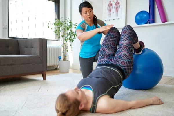 Chinese vrouw personal trainer tijdens een workout sessie met een aantrekkelijke blonde cliënt in een licht medisch kantoor — Stockfoto