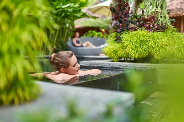 발리에서 열대 휴가 기간 동안 고급스러운 호텔의 햇볕이 잘 드는 무성한 돌 수영장에서 야외에서 휴식을 취하는 아름다운 평화로운 여성 — 스톡 사진