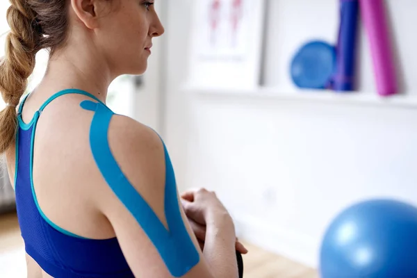 Attractive blond woman in a bright sport therapy office with kinesio tape on her neck and shoulder to heal pain — Stock Photo, Image