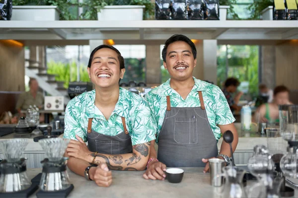 Lifestyle portret van twee vriendelijke glimlachende Balinese duizendjarige barista's die trendy kleding en schorten dragen in hipster café waar fair-trade koffie wordt geserveerd — Stockfoto