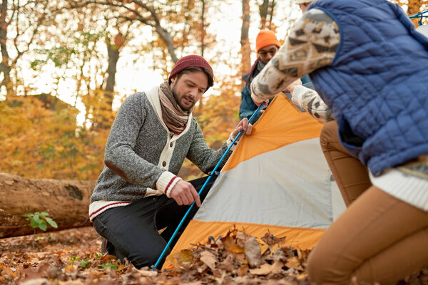 Группа канадских туристов устанавливает палатку в осеннем лесу
