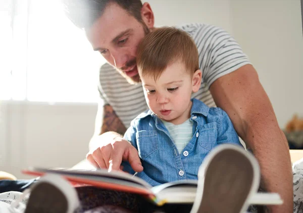 Schattig, jong vrouwtje peuter leren lezen boek met knappe duizendjarige vader op bed — Stockfoto