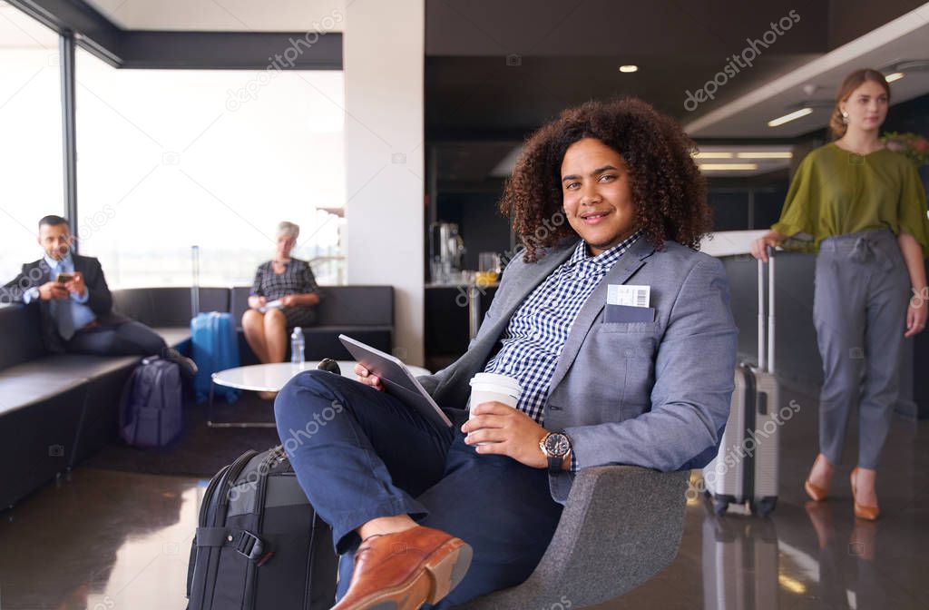 African american man waiting for flight sitting in modern airport lounge on tablet with luggage