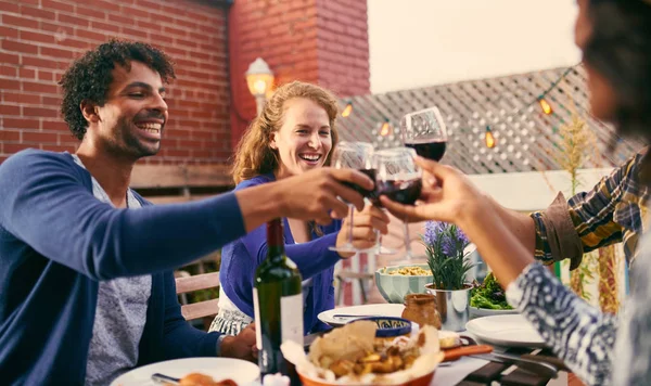 Grupo de amigos diversos jantando e um copo de vinho ao ar livre em ambiente urbano — Fotografia de Stock