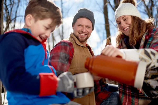 Семья с сыном наслаждаются игрой в свежем снегу зимой и горячим шоколадом во время пикника — стоковое фото