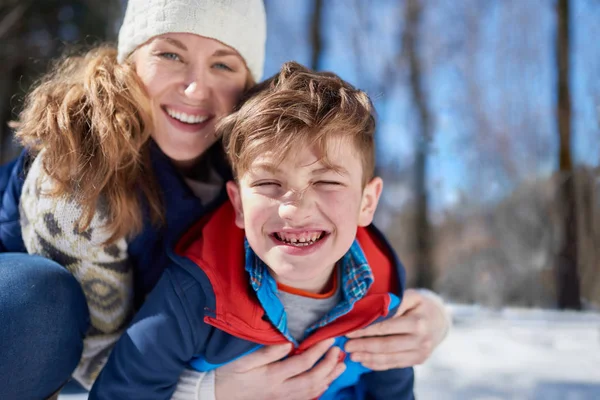 Madre e hijo disfrutando jugando en nieve fresca durante el invierno y compartiendo un abrazo — Foto de Stock