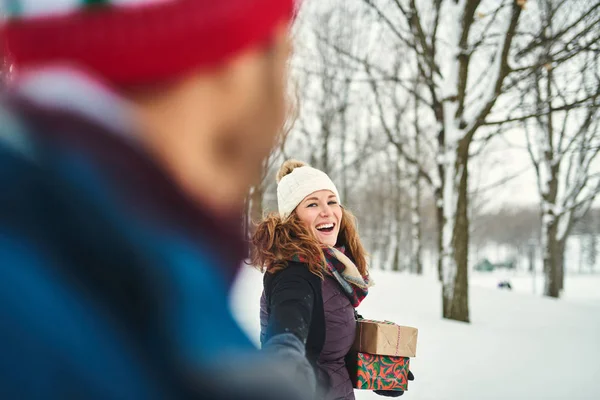 Улыбающаяся пара с рождественскими подарками во время прогулки по зимнему лесу — стоковое фото