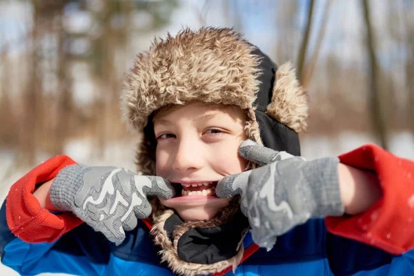 Retrato de un niño sonriente siendo tonto y tirando de una cara en nieve fresca durante el invierno — Foto de Stock