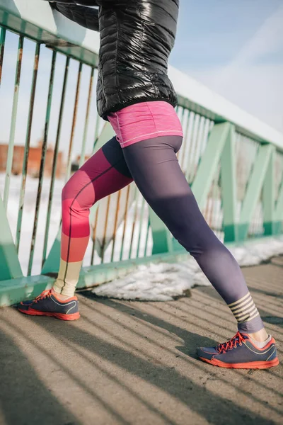Healthy caucasian woman keeping fit in the winter by stretching before jogging in a snow filled city — Stock Photo, Image