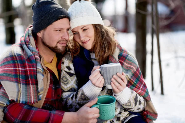 Пара влюбленных наслаждается нежным моментом в свежем снегу зимой и пьет горячий шоколад вместе — стоковое фото