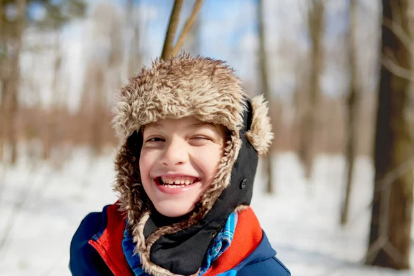 Retrato de un niño sonriente disfrutando jugando en nieve fresca durante el invierno y usando un sombrero de piel recortada — Foto de Stock
