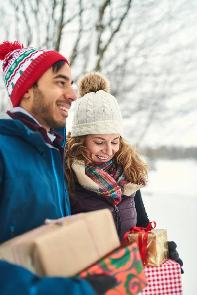 Улыбающаяся пара с рождественскими подарками во время прогулки по зимнему лесу — стоковое фото