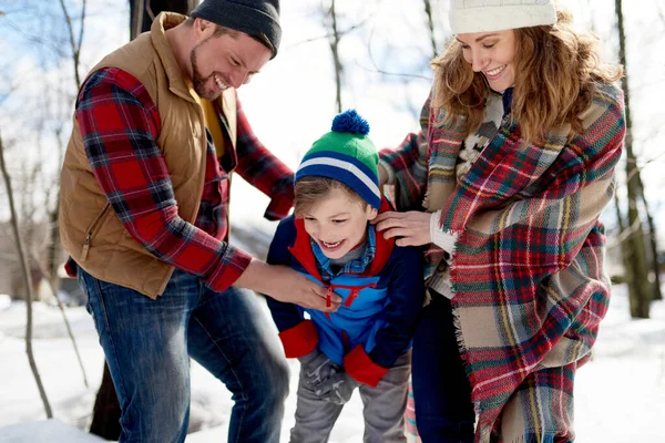 Madre y padre disfrutando jugando en nieve fresca durante el invierno y haciendo cosquillas a su hijo mientras ríen — Foto de Stock