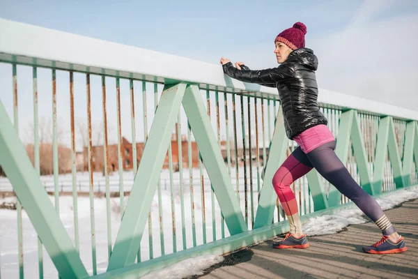 건강 한 백인 여성 이 눈으로 가득 찬 도시에서 조깅을 하기 전에 몸을 뻗어 겨울에 잘 적응하고 있다 — 스톡 사진