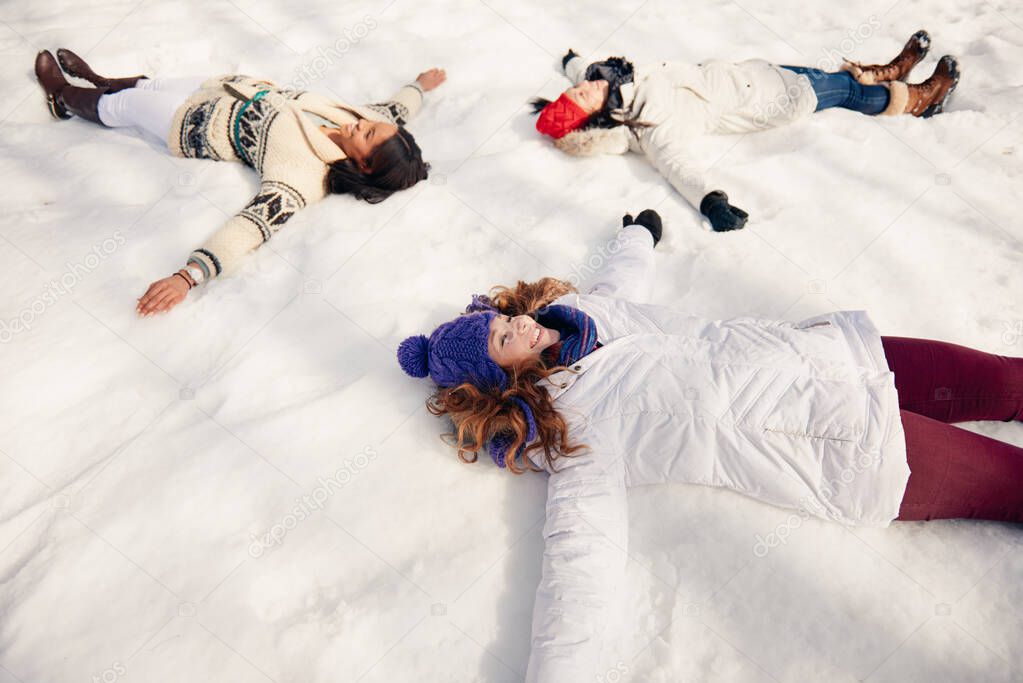 Group of girl friends making snow angels in winter