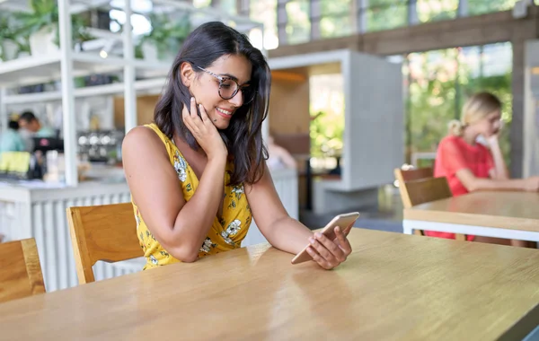 Modern ve parlak bir kafede, gülümseyen İspanyol modacının cep telefonuyla bitkilerle fotoğraf çektiği samimi bir yaşam tarzı portresi. — Stok fotoğraf