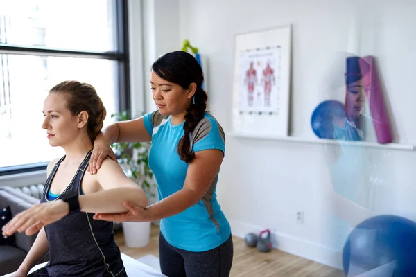 Chinese woman physiotherapy professional giving a treatment to an attractive blond client in a bright medical office — Stock Photo, Image