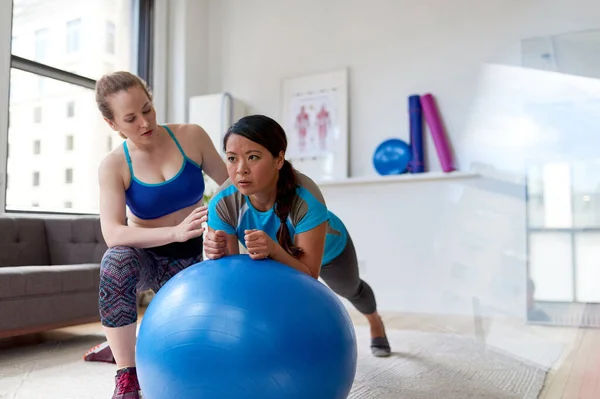 Blanke vrouw fysiotherapeut geven een workout sessie aan een mid-Adult Chinese vrouwelijke patiënt op een stabiliteits bal — Stockfoto