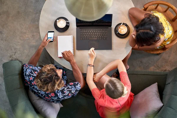 Candid toma aérea de tres compañeros de trabajo milenarios multiétnicos que colaboran en el café con el ordenador portátil en el café brillante que sirve café de comercio justo — Foto de Stock