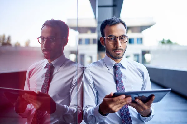 Millenial businessman leaning confidently on a dark glass wall w — Stock Photo, Image