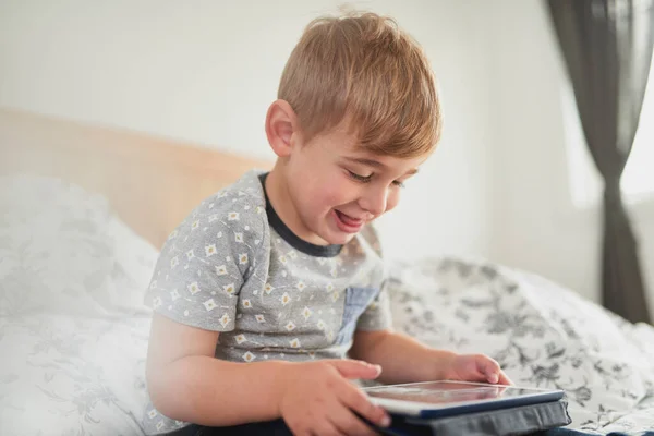 Porträt eines jungen glücklichen männlichen Kindes mit digitalem Tablet im Bett — Stockfoto
